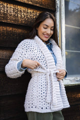 person wearing a cream-colored V-stitch crocheted openwork cardigan tied at the waist against a wood-paneled background thumbnail