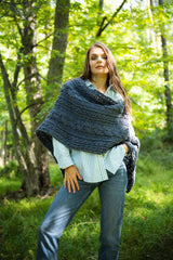 person wearing a dark grey textured cable-knit buttoned wrap shawl with cuffed sleeves against a lush green wooded background thumbnail