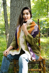 person wearing a multicolored ripple-pattern scarf over an olive green jacket and jeans thumbnail