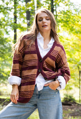 person wearing a striped brown and plum button-front knit cardigan, white shirt, and jeans outdoors in a wooded setting thumbnail