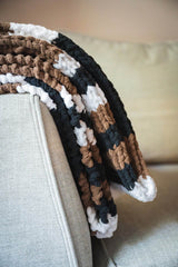 folded black, brown, and white striped blanket draped over a couch. thumbnail