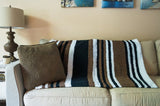 black, brown, and white striped blanket draped over a couch. thumbnail