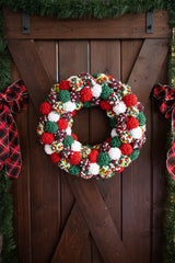 Pom-pom wreath in Christmas colors hanging on wood door.  thumbnail