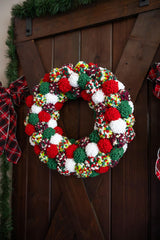 Pom-pom wreath in Christmas colors hanging on wood door.  thumbnail