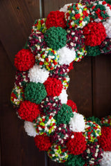 closeup of Pom-pom wreath in Christmas colors hanging on wood door.  thumbnail