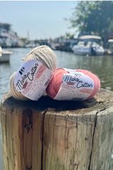 Two skeins, 1 tan, 1 coral, of mako cotton yarn on a dock next to water with boats in the background. thumbnail