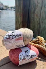 Two skeins, 1 tan, 1 coral, of mako cotton yarn on a dock next to water with boats in the background. thumbnail