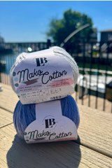 One grey and one blue ball of Mako Cotton Yarn on a deck with the water in the background thumbnail