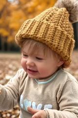 baby wearing mustart crochet hat with pom pom thumbnail