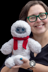 woman holding a handmade fluffy white yeti amigurumi toy with a red scarf and grey face thumbnail