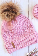 angled flat lay of crochet hat with heart pattern and faux fur pom pom thumbnail