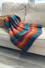 colorful crocheted throw blanket in colorful self-striping yarn draped over a couch thumbnail