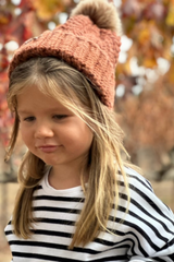 child wearing rust colored crochet hat with fur pom pom thumbnail
