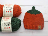 knitted orange pumpkin beanie with orange and green yarn skeins thumbnail