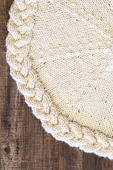 cream knitted Christmas tree skirt with a braided cable border flat laid on dark wood thumbnail