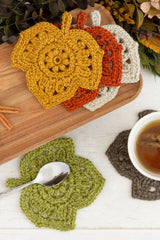 crocheted leaf-shaped coasters in autumn colors on a wooden board next to a cup of tea thumbnail