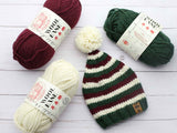 striped elf stocking cap with red, white, and green stripes and a white pom-pom, surrounded by matching skeins of yarn thumbnail