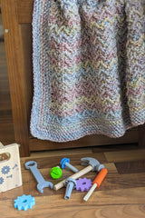crochet baby blanket using herringbone textured stitch with kids toys on floor thumbnail