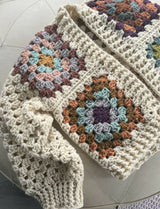 close-up of a cream crocheted granny square cardigan with colorful yarn motifs thumbnail