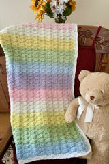 pastel rainbow crocheted baby blanket draped on a chair with teddy bear thumbnail