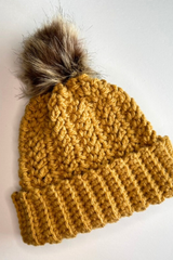 flat lay of mustard hat with fur pom pom thumbnail