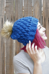 woman wearing a teal alpine stitch crochet beanie with a faux fur pom pom outdoors thumbnail