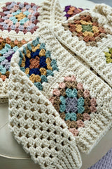 close-up of a cream crocheted granny square cardigan with colorful yarn motifs thumbnail