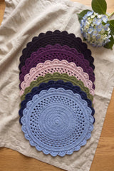 stacked crocheted round placemats with scalloped edges in various colors flat laid on a beige cloth next to flowers thumbnail