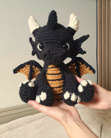 crochet amigurumi stuffed animal of a dragon being held up by adult hands thumbnail