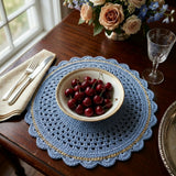 blue crocheted round placemat with gold accent detail set on a wooden table with a bowl of cherries, silverware, and glass goblet thumbnail