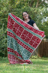 woman holding a handmade mosaic crochet blanket featuring snowflake squares in red green and white yarn outdoors thumbnail