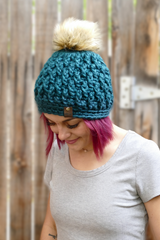 person wearing a teal alpine stitch crochet beanie with a faux fur pom pom outdoors thumbnail