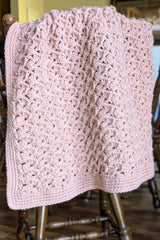 pink crochet baby blanket draped over chair thumbnail