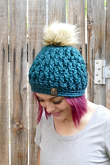 person wearing a teal alpine stitch crochet beanie with a faux fur pom pom outdoors thumbnail
