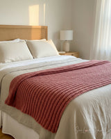 dusty pink knitted mistake rib throw blanket draped on a bed thumbnail
