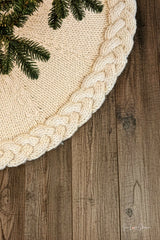 cream knitted Christmas tree skirt with a braided cable border flat laid on dark wood thumbnail