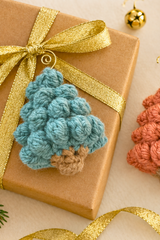 handmade teal bobble stitch Christmas tree ornament resting on a wrapped gift thumbnail