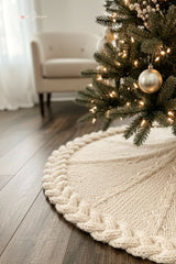 cream knitted Christmas tree skirt with a braided cable border lying under a decorated Christmas tree on light wood flooring thumbnail