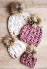 handmade white and dusty rose textured crochet beanies with faux fur pom-poms on a wooden surface thumbnail