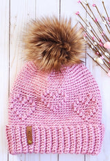 flat lay of crochet hat with heart pattern and faux fur pom pom thumbnail