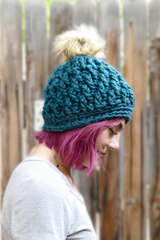 person wearing a teal alpine stitch crochet beanie with a faux fur pom pom outdoors thumbnail