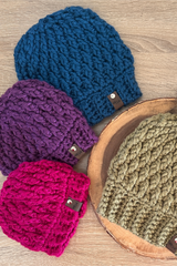 four alpine stitch crochet beanies in blue purple pink and green stacked on a wooden surface thumbnail
