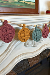 crocheted autumn leaf garland with wooden beads hanging across a mantelpiece thumbnail